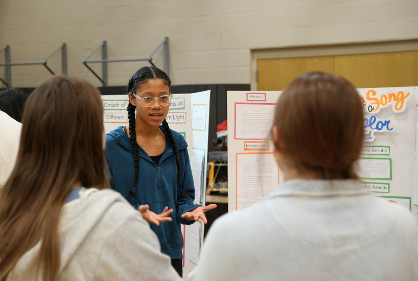 student stands next to a poster board, presenting her science project at Spartan Day of Science